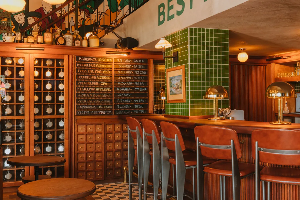 Vitrina de cervezas artesanales en estantería de madera junto a la barra, con columna revestida en azulejo verde