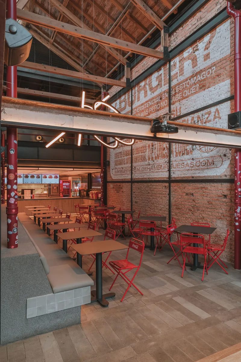 Salón de Universal de Hamburguesas con sillas rojas, mesas de madera y un mural pintado sobre ladrillo visto
