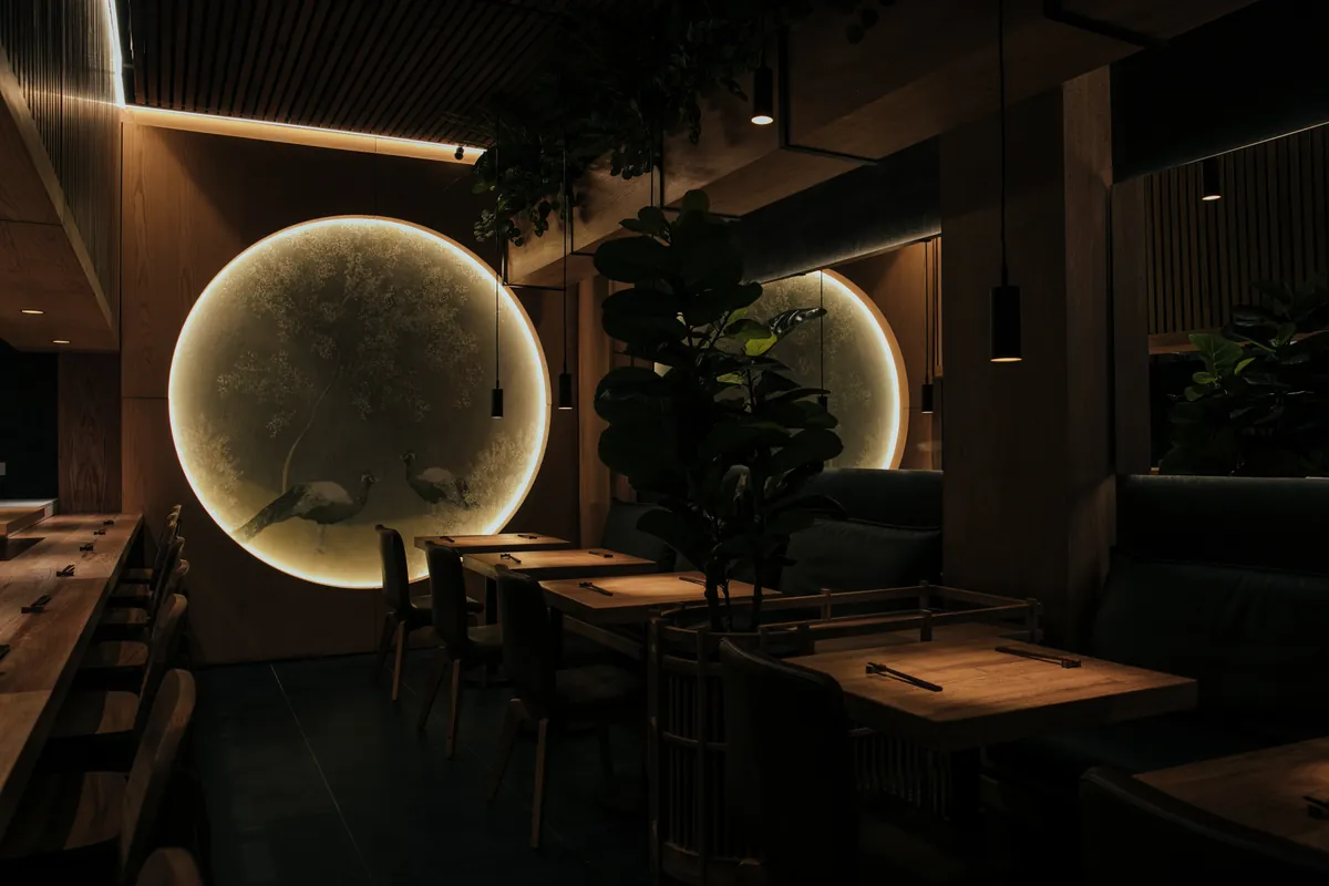 Nicho circular retroiluminado con ilustración de aves sobre un panel de madera, junto a una planta de higuera