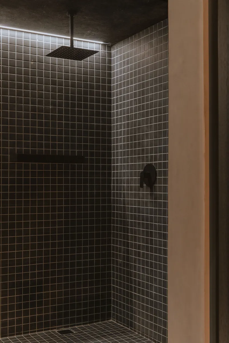 Ducha revestida en mosaico negro con grifería de cabezal cuadrado y accesorios de latón