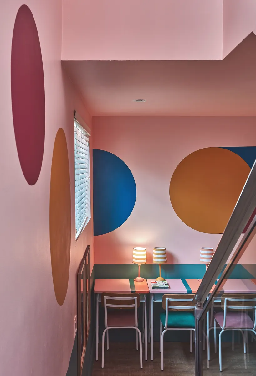 Comedor en tonos rosa con paredes pintadas en círculos azules, dorados y granates junto a lámparas de mesa
