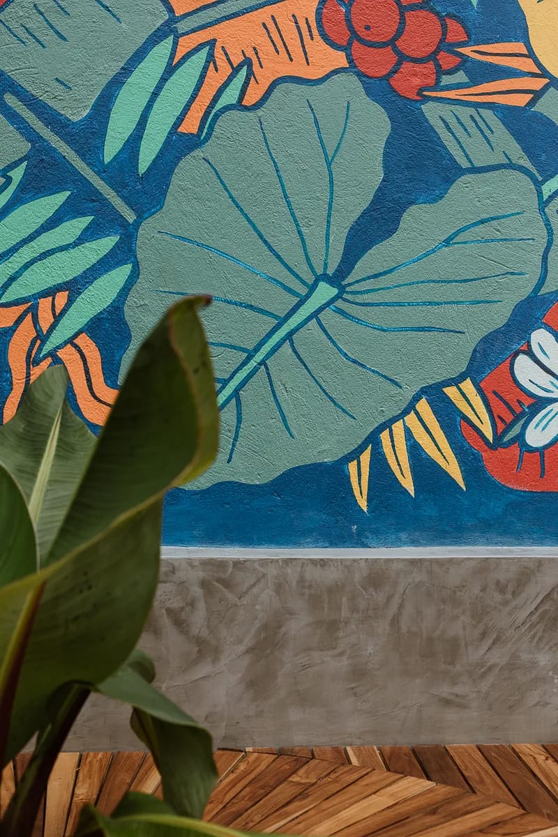 Detalle del mural tropical pintado a mano en tonos verdes, rojos y azules sobre el patio de Colo Coffee Usaquén