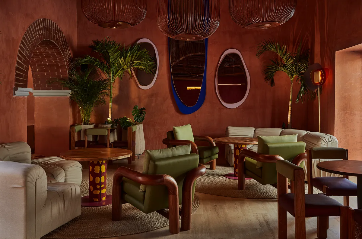 Salón con sofá y sillones de cuero verde junto a una mesa redonda de madera bajo arcos de piedra