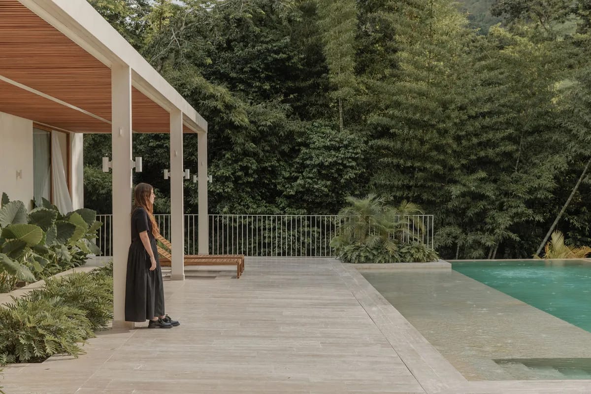 Mujer de pie bajo el corredor cubierto de Casa N, con vista a la piscina y al bosque de guadua