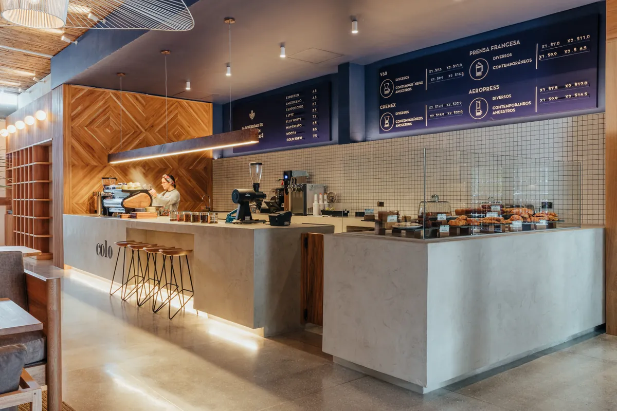 Barra de café en concreto con equipos de espresso y menú iluminado sobre azulejo blanco