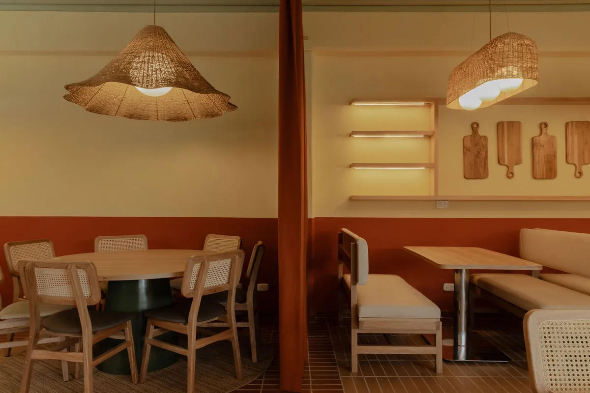 Comedor con mesa redonda y sillas de mimbre bajo una lámpara de fleco tejida junto a una cortina terracota