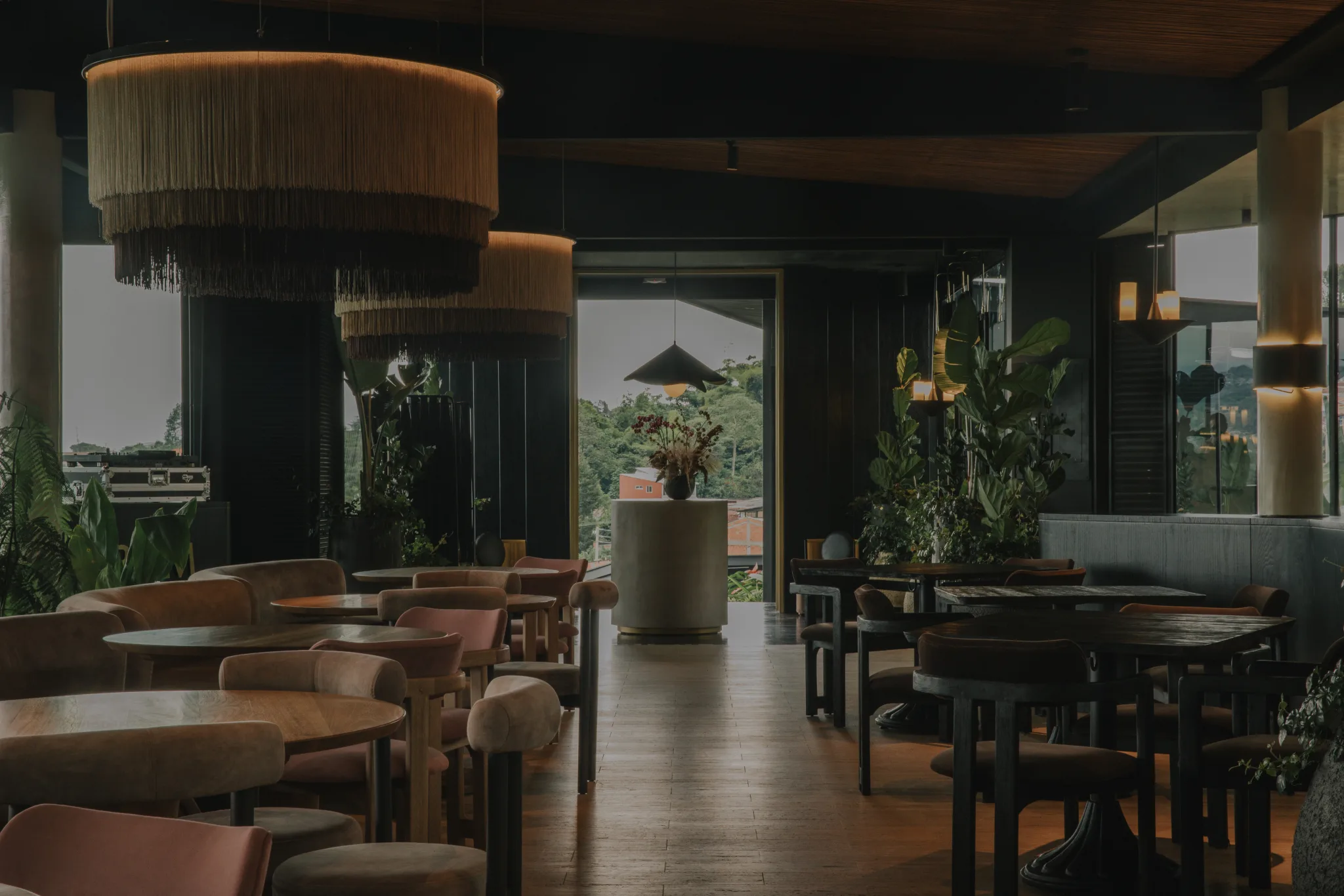 Salón de restaurante con lámparas colgantes de fleco en fibra natural, sillas tapizadas en terracota y un ventanal abierto al jardín