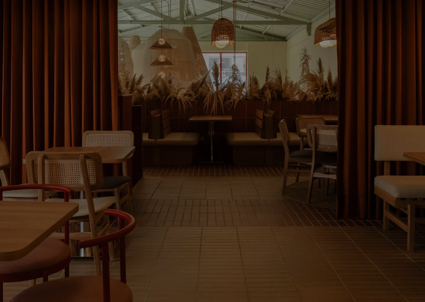 Comedor de restaurante con cortinas en terracota y luminarias artesanales de mimbre colgando del techo