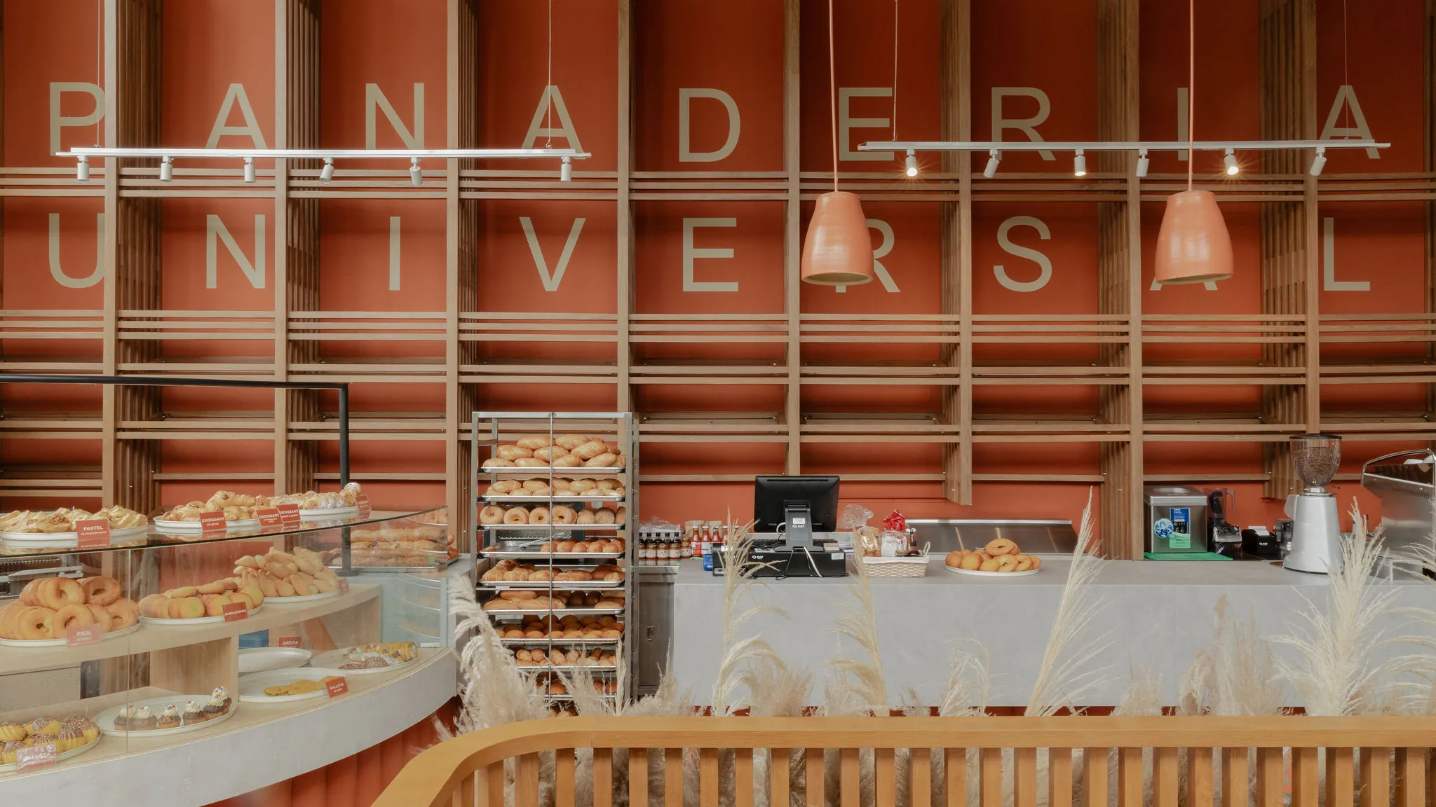 Muro de madera ranurada en tonos terracota con el rótulo Panadería Universal y lámparas de cerámica colgantes