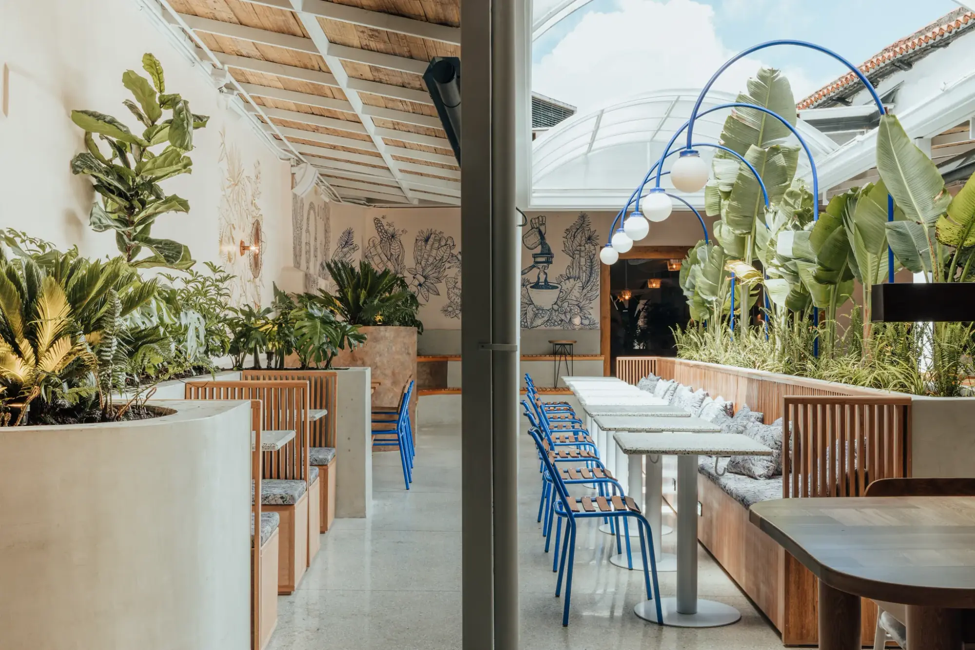 Terraza cubierta de Colo Coffee Andes con banca de concreto, plantas tropicales y estructura de arcos azules con lámparas colgantes