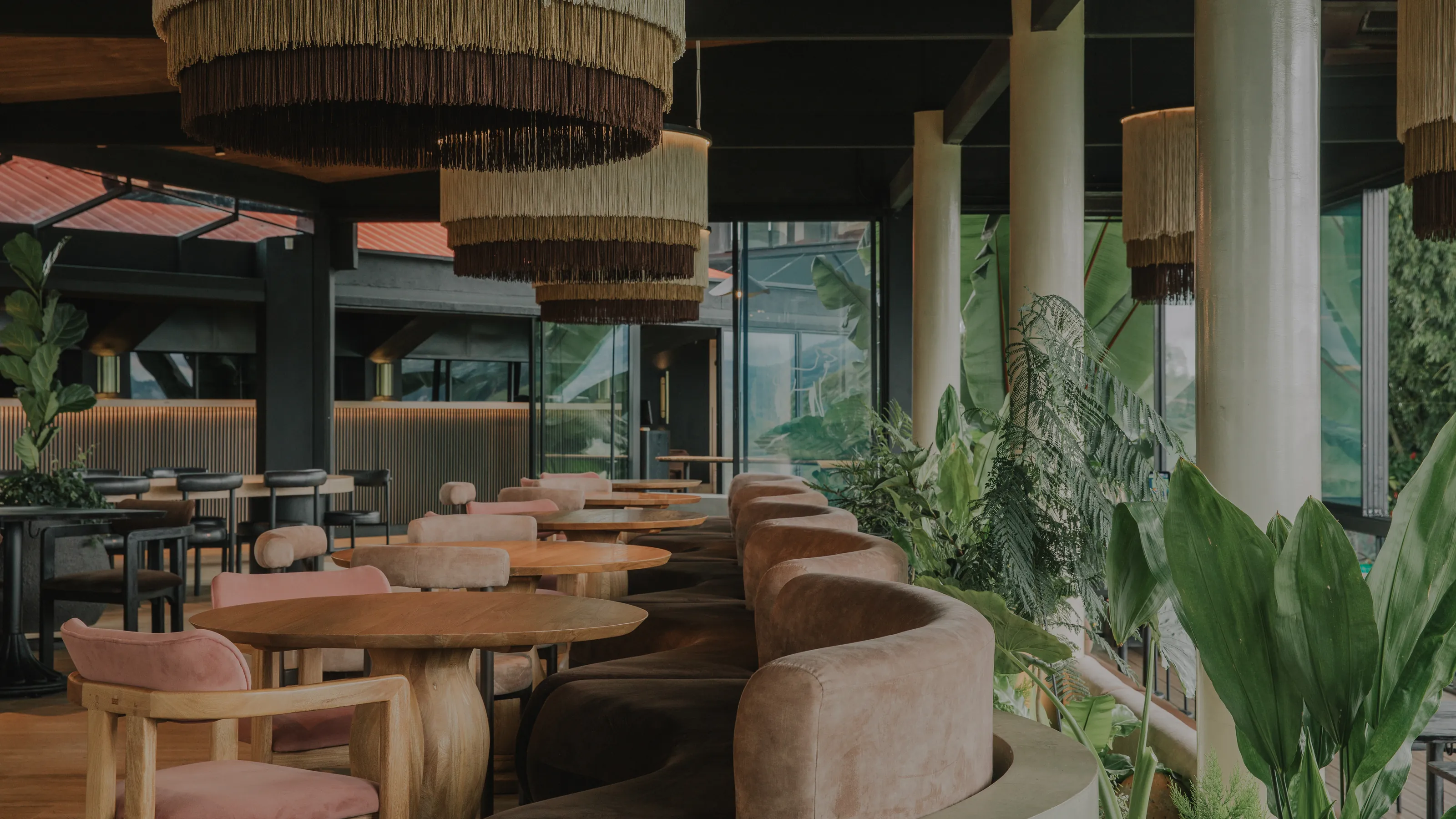 Barra de café con lámparas artesanales de fibra natural, arcos revestidos en madera y taburetes rojos frente a mesas redondas