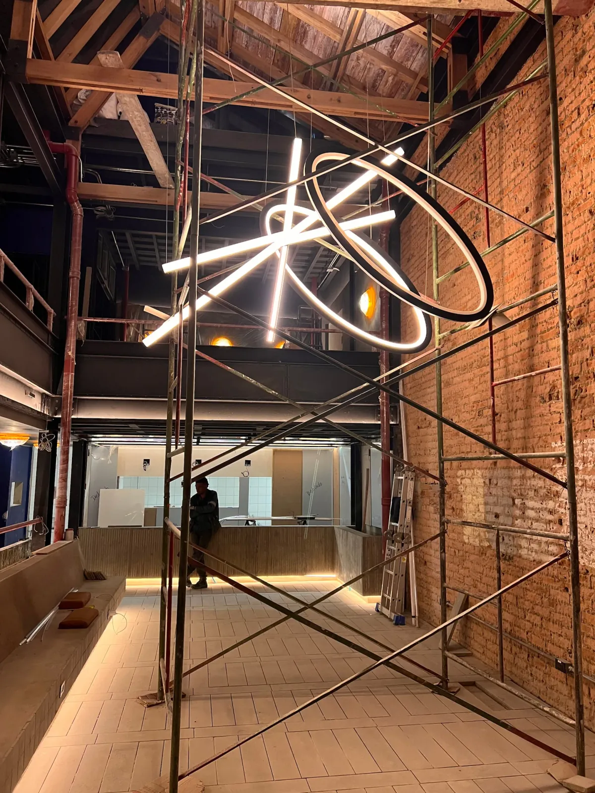 Supervisión de obra en un local en construcción, con andamios y una instalación lumínica suspendida sobre el mostrador
