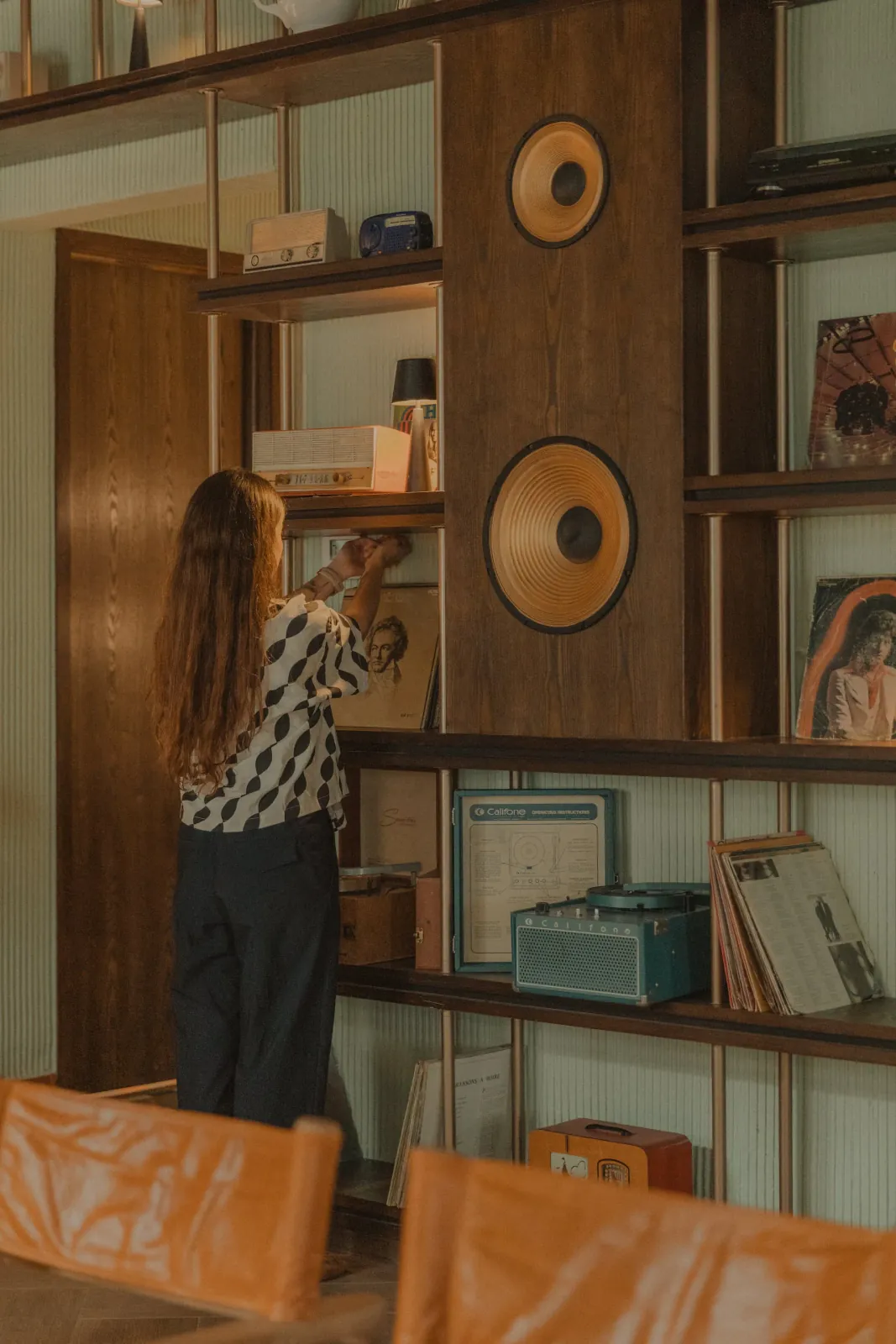 Estilista acomodando vinilos y objetos vintage en una repisa de madera como último nivel de detalle antes de la entrega